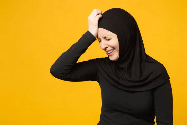 Sad upset crying confused young arabian muslim woman in hijab black clothes posing isolated on yellow wall background, studio portrait. People religious Islam lifestyle concept. Mock up copy space
