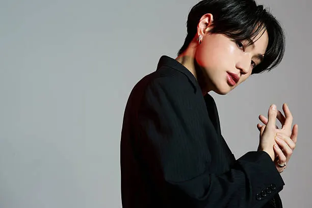 Portrait shot of a young Asian man wearing a suit and makeup against a gray background