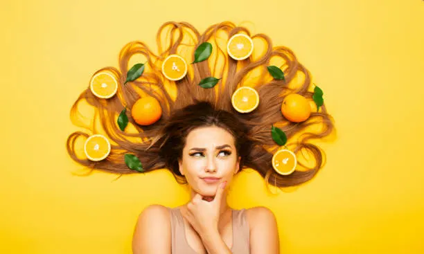 beautiful girl lying on studio background with orange fruits lay out on long hair, young woman head thinking, making choice, view from above